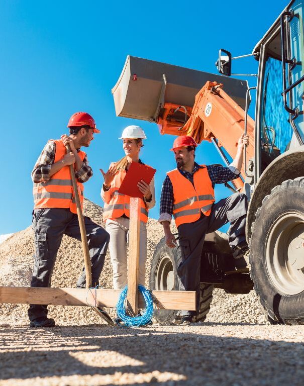 tre operatori in un cantiere parlano vicino a una ruspa