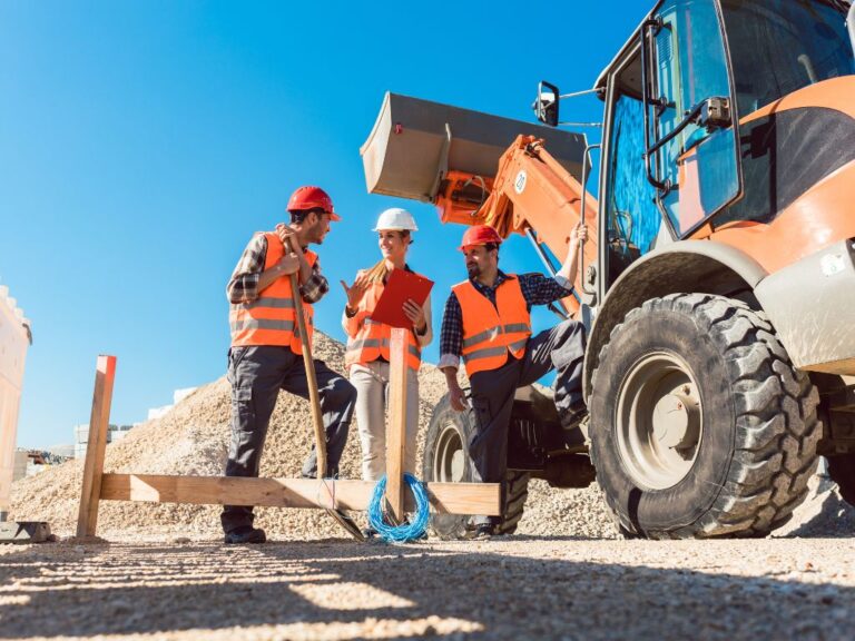 tre operatori in un cantiere parlano vicino a una ruspa